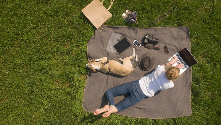 A woman works outside on her computer with her dog