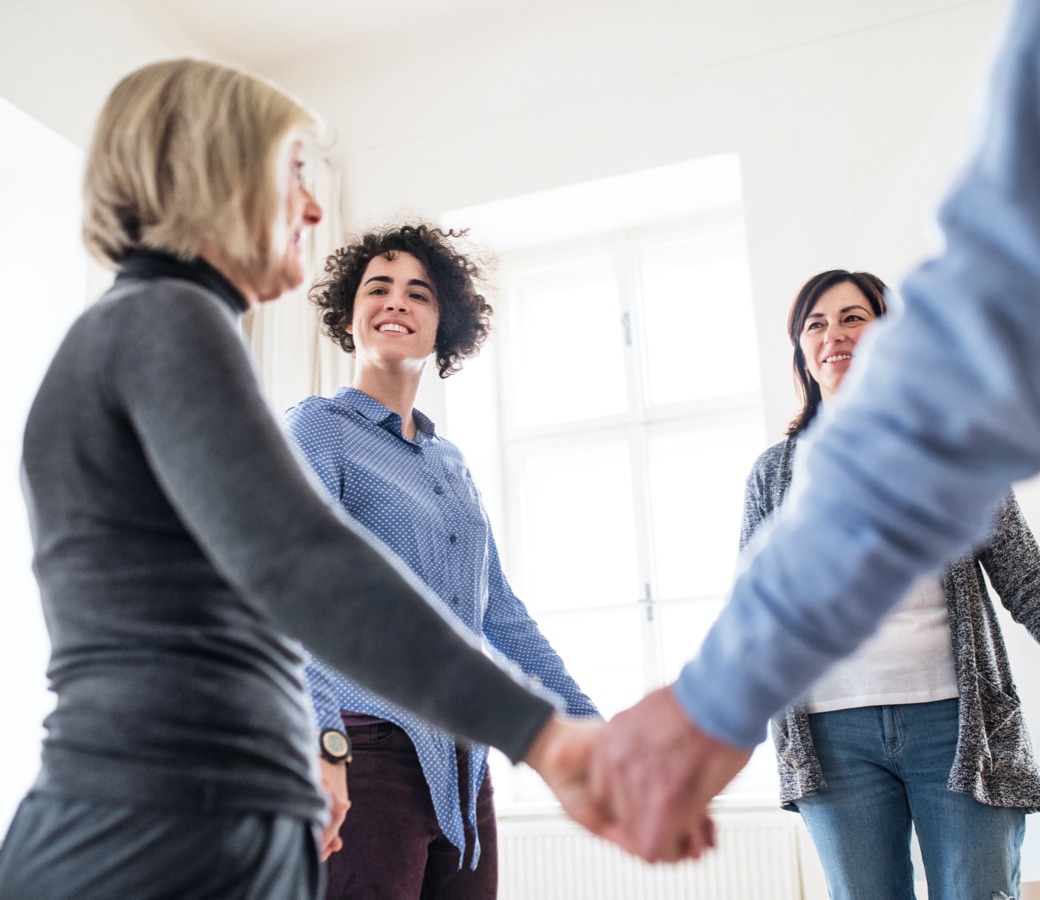 Group of people joining hands during a support group for people affected by addiction
