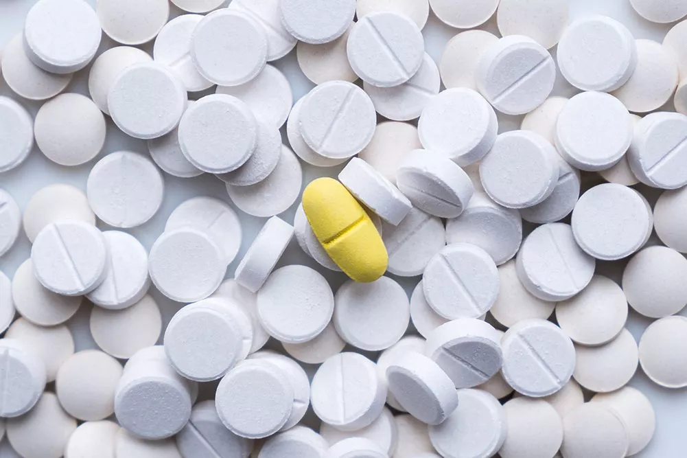 A pile of white naltrexone pills with one yellow pill in the middle
