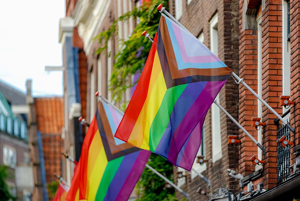 Pride flags are displayed outside brick houses in a neighborhood