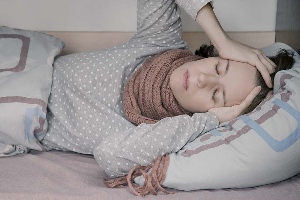 a woman lays on a couch bundled up clutching her head while suffering methadone withdrawal symptoms