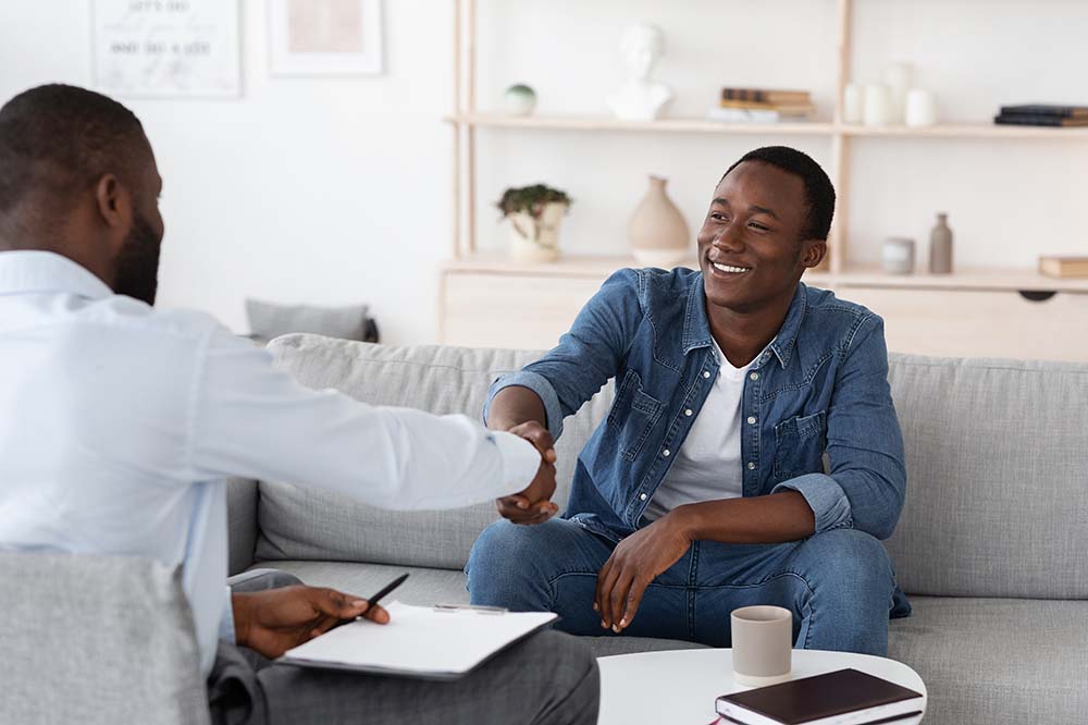 A young man on his addiction recovery journey shakes hands with a clinician