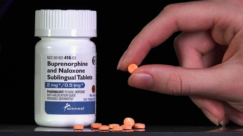 A suboxone pill is held between fingers next to a bottle of suboxone