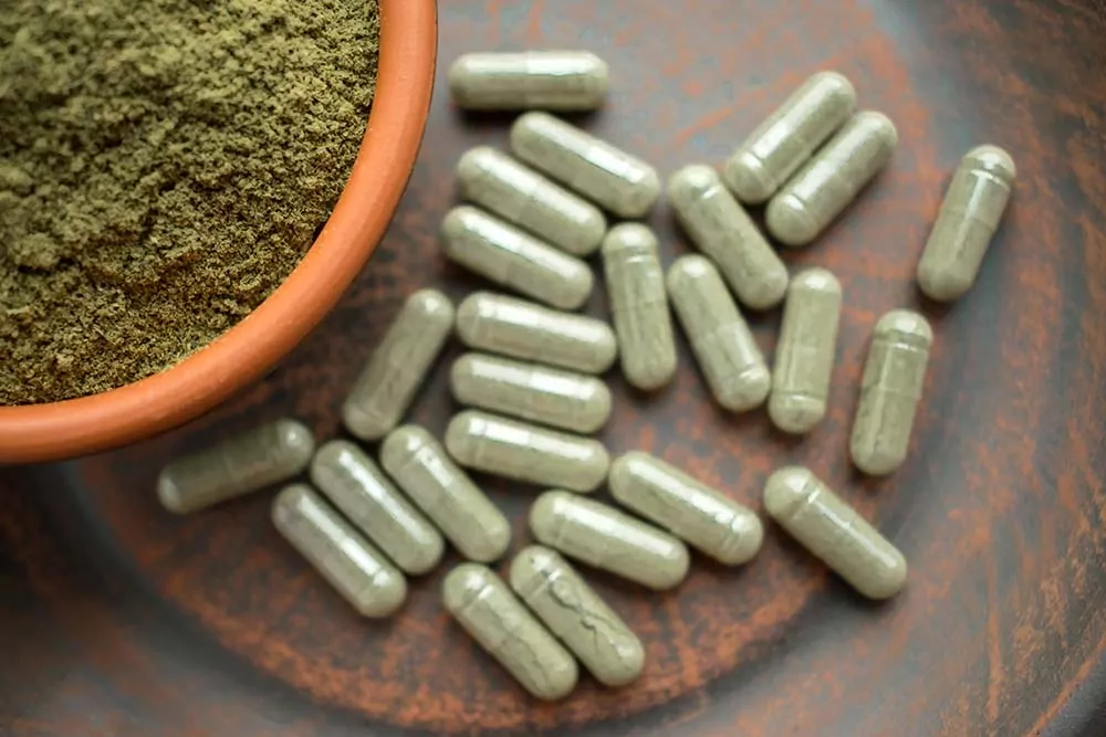 Kratom pills next to a bowl of kratom powder